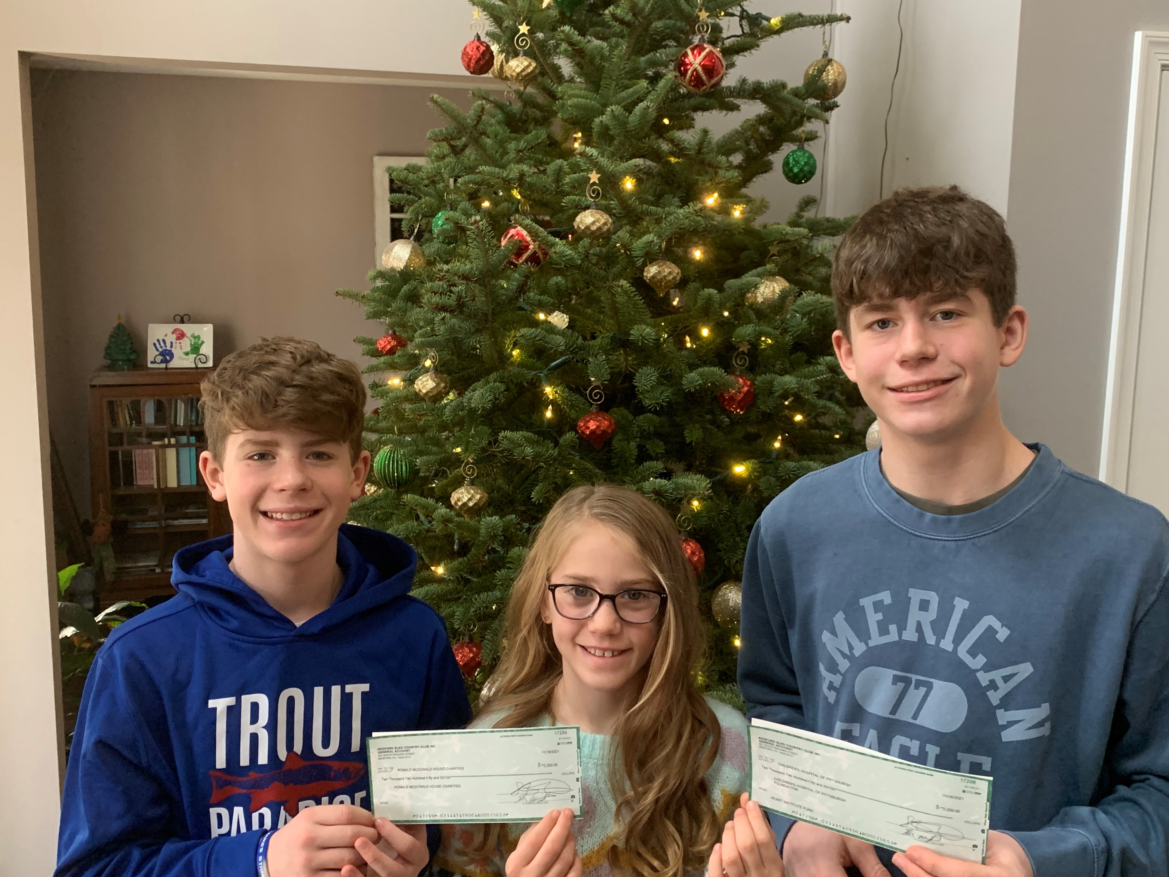 Owen and his siblings holding checks from the golf fundraising event