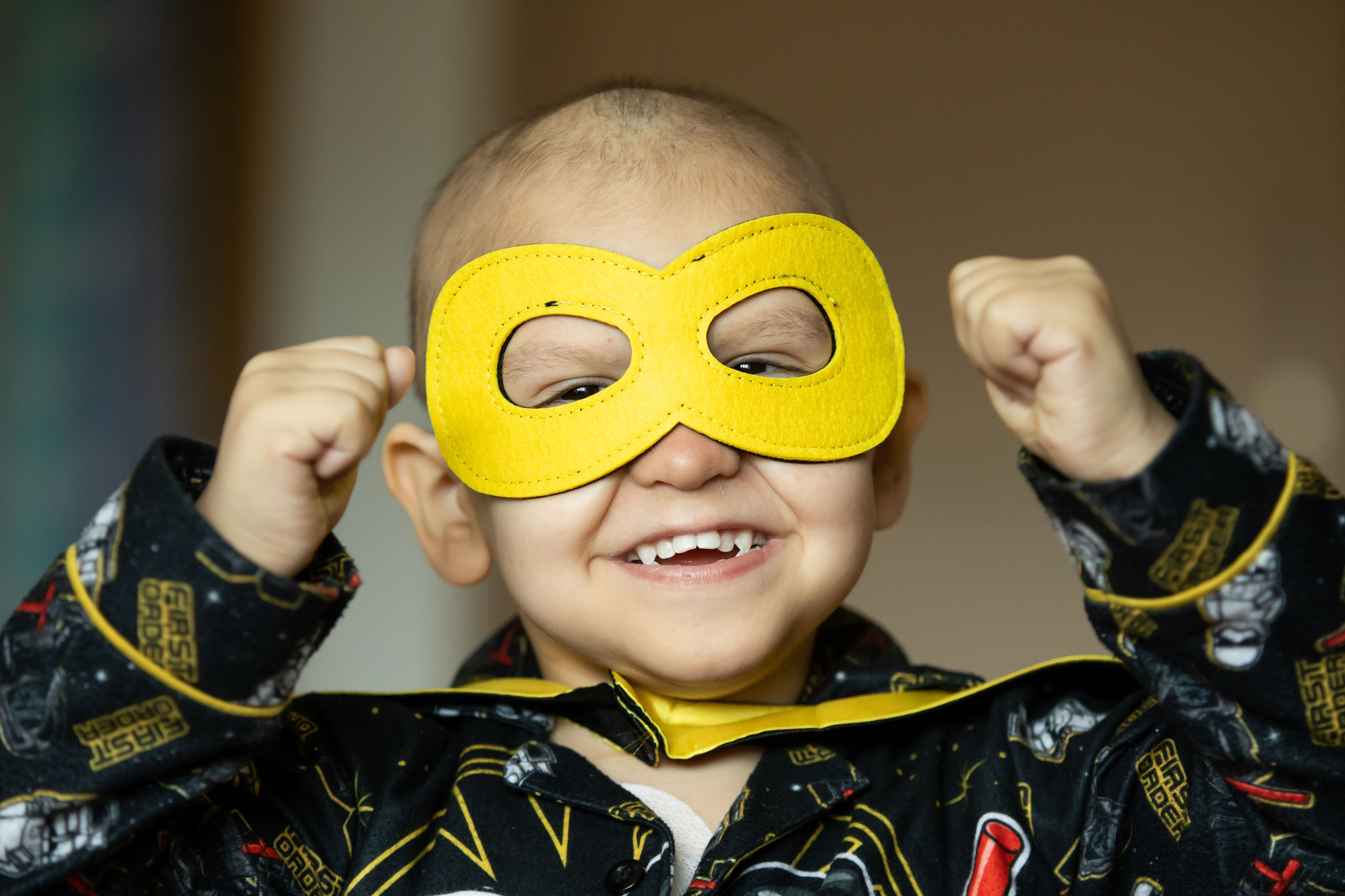 boy in superhero mask smiles while doing strong arm pose